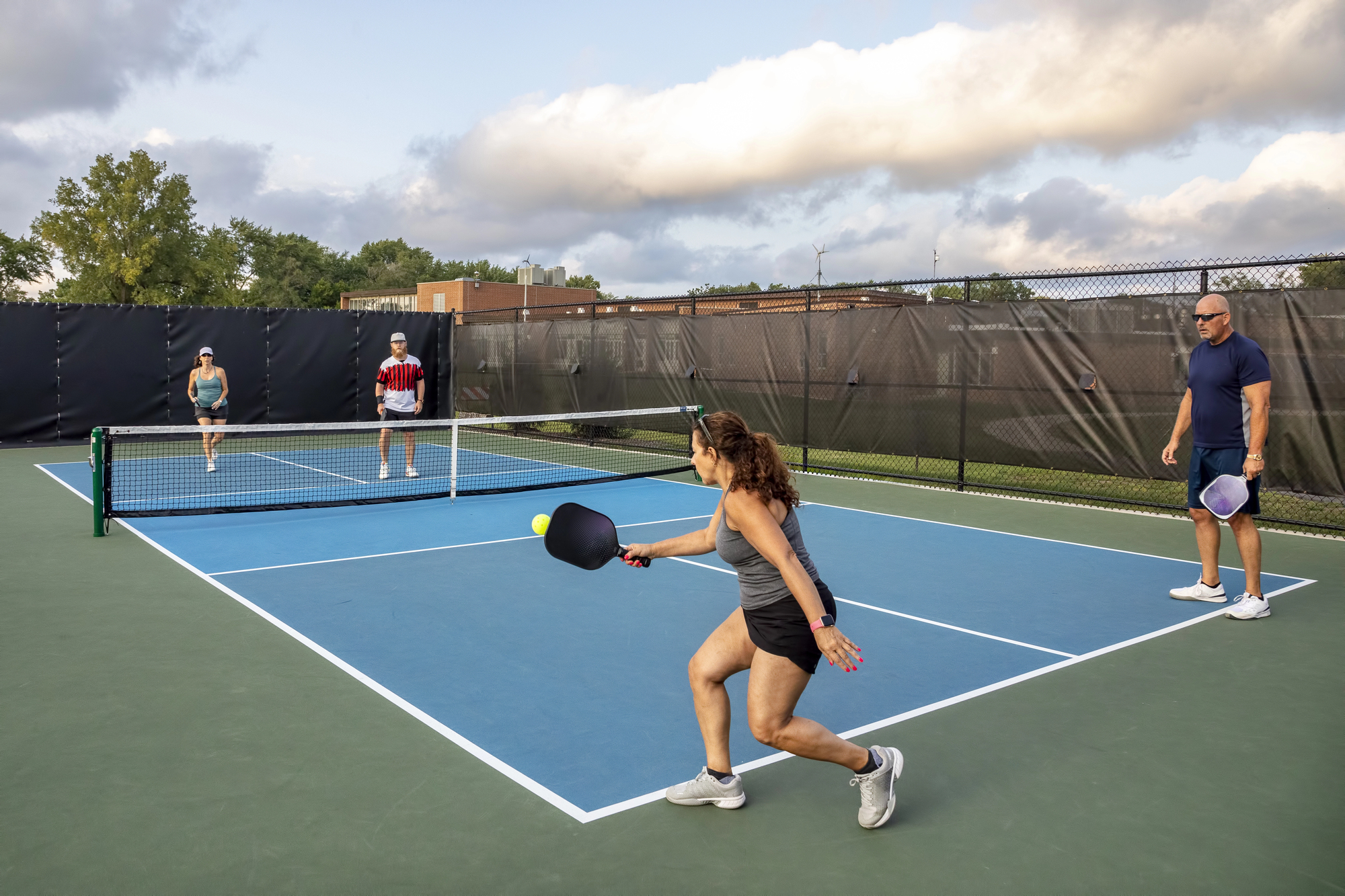A female pickleball player returns a ball as her partner watches in a mix doubles match.