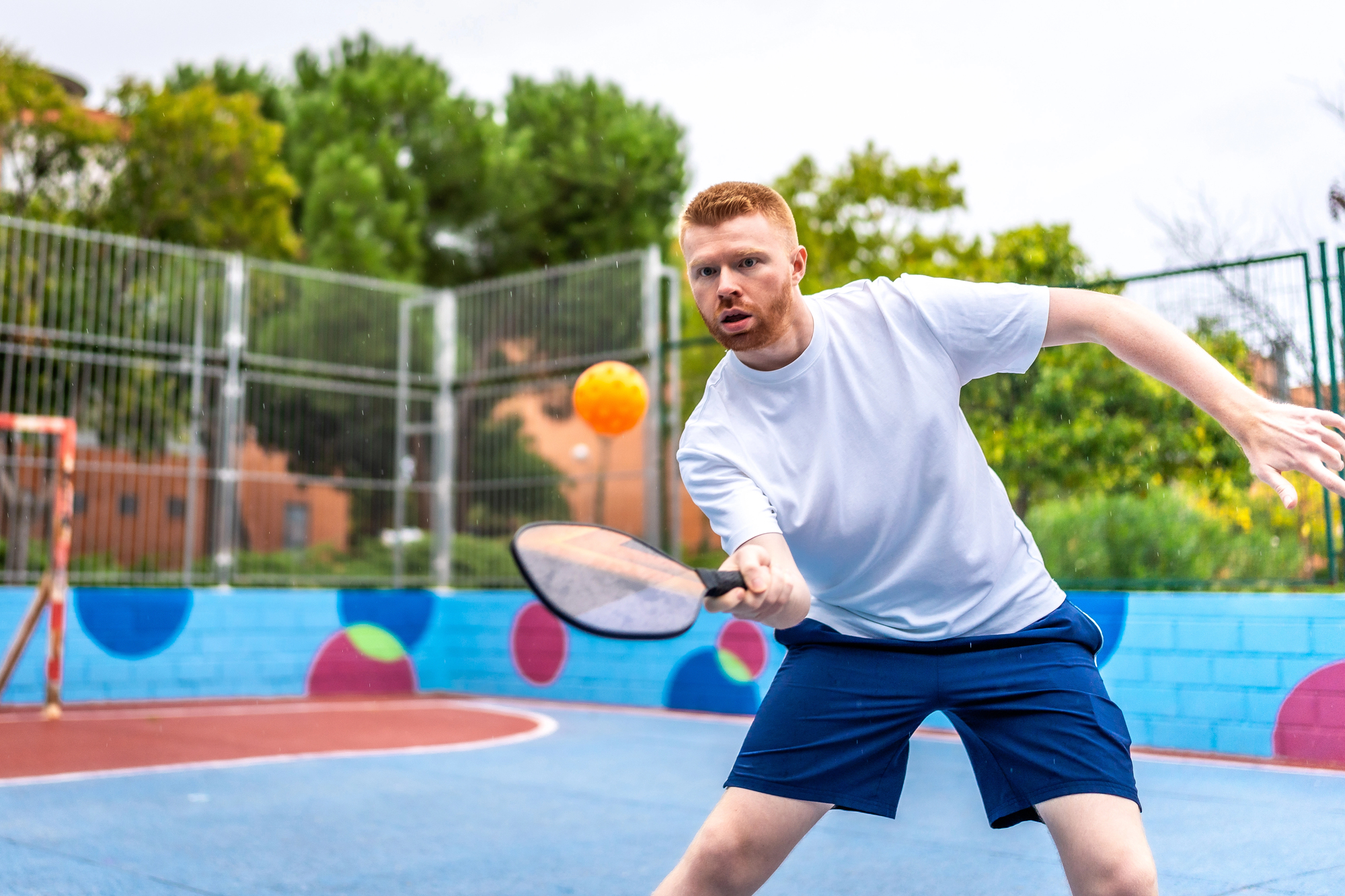 Energetic sportive young caucasian man playing pickelball in a colorful outdoor pitch.