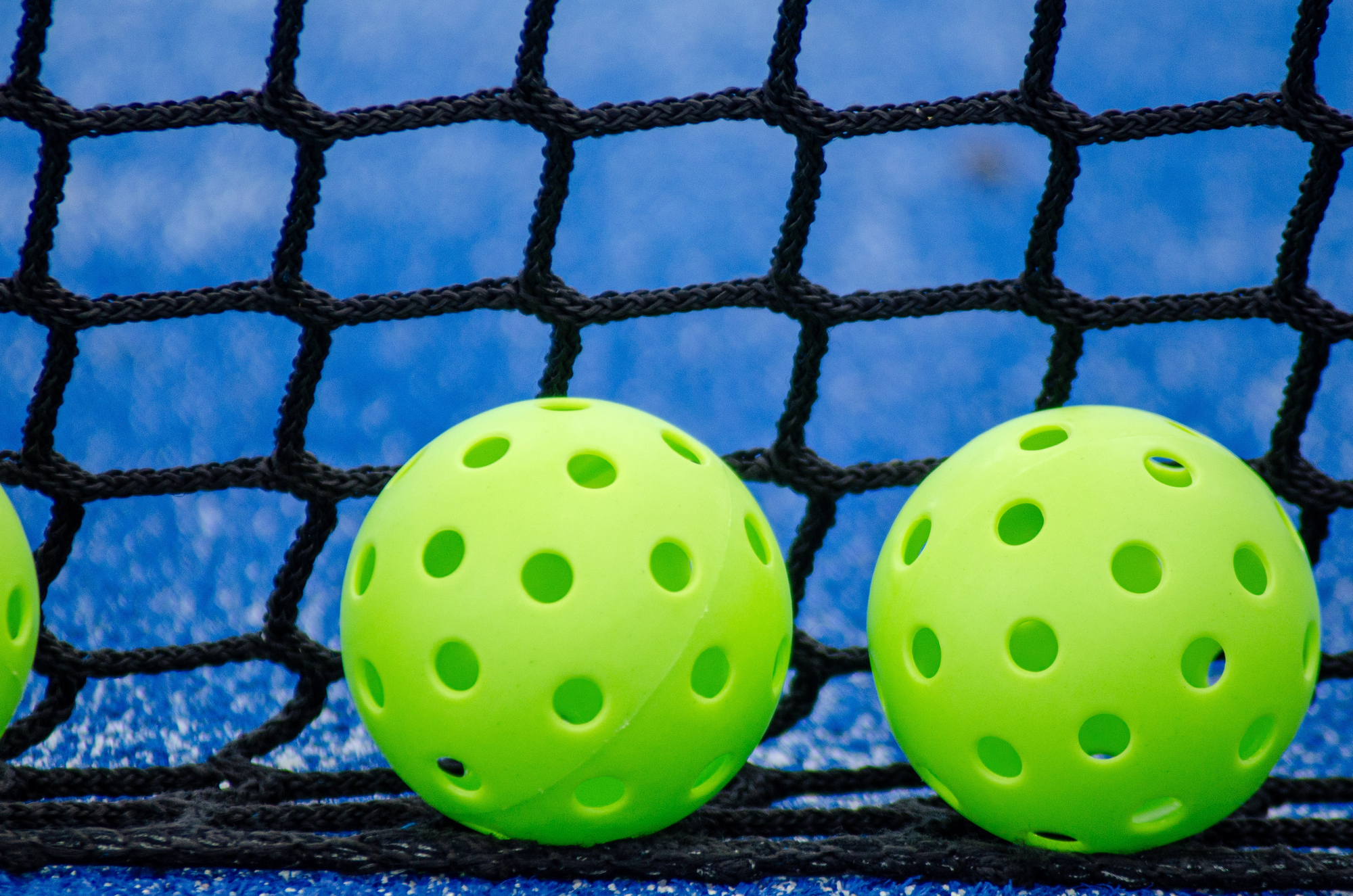 Two green pickleball ball near the court in a picklebal field, blue background.