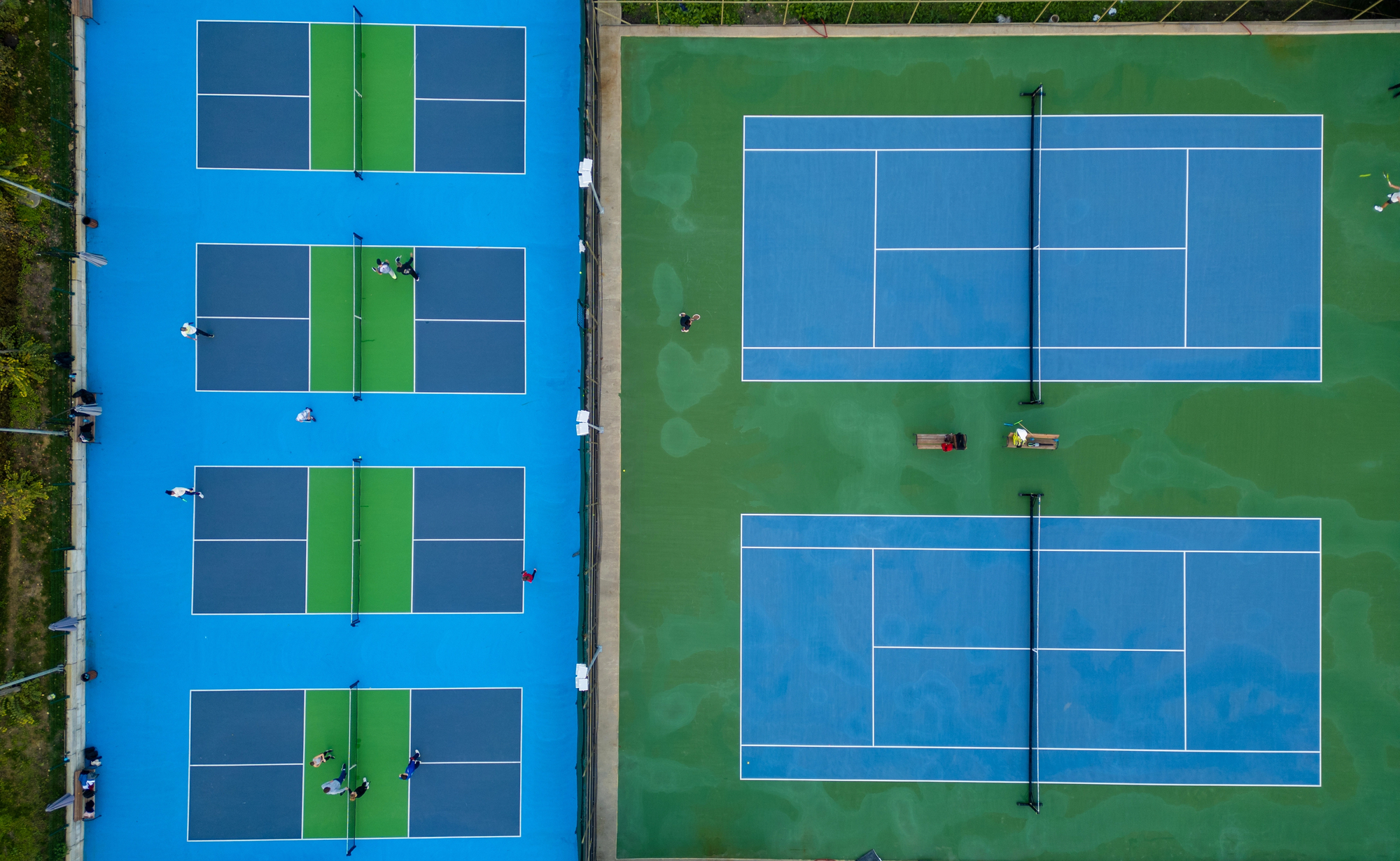 Aerial view of multiple pickleball courts with players in action. Colorful blue and green outdoor sports complex on a sunny day. Recreational activity and healthy lifestyle concept.