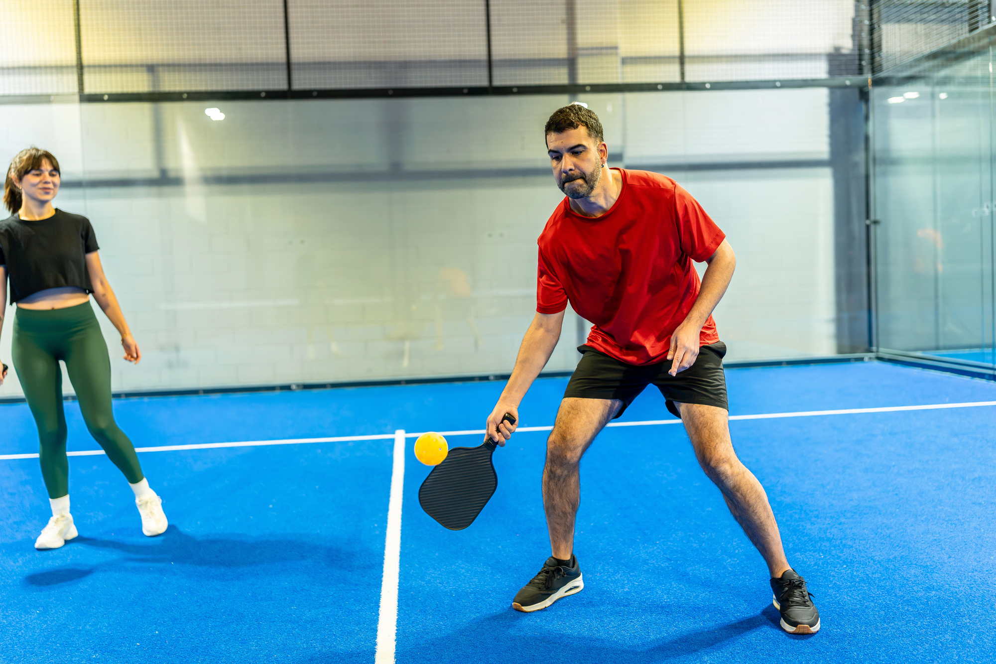 Two players competing in a dynamic indoor pickleball match on a blue court with white lines, showing athletic movement, focus, and recreational fitness for active lifestyles