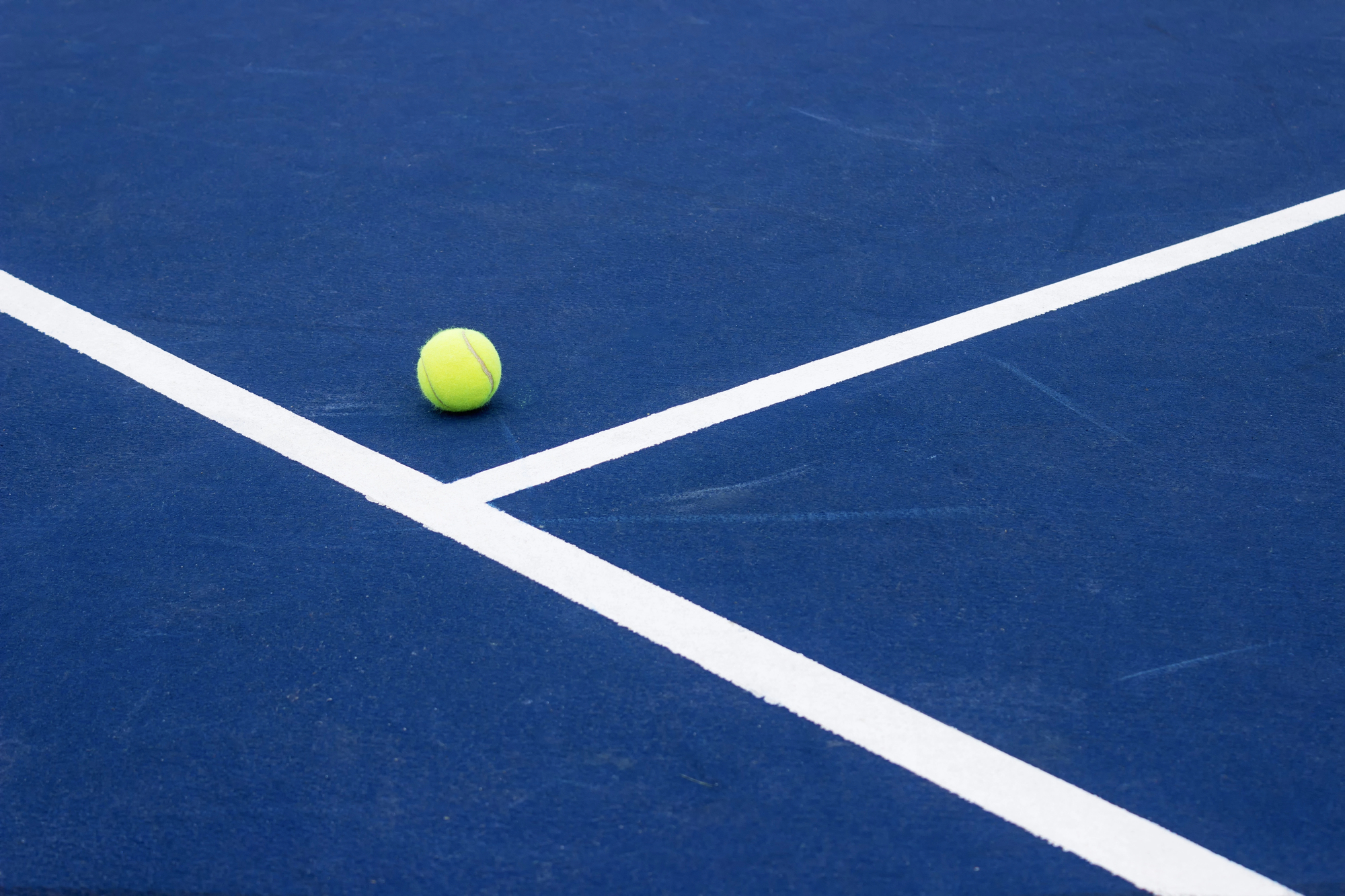 Tennis ball resting on a blue tennis court line