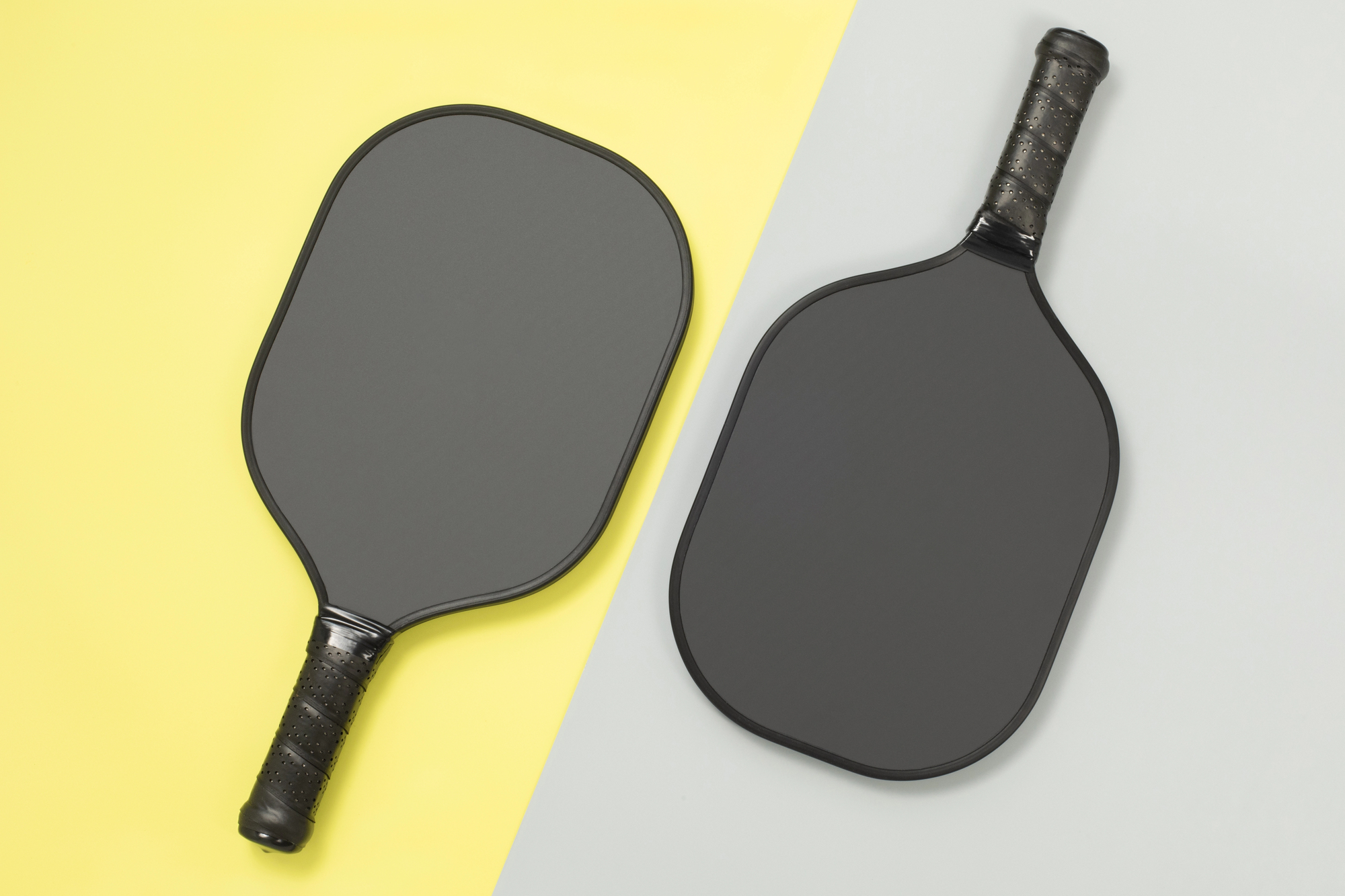 Close top view of two black pickleball paddles on yellow and gray background. Sport game competition concept